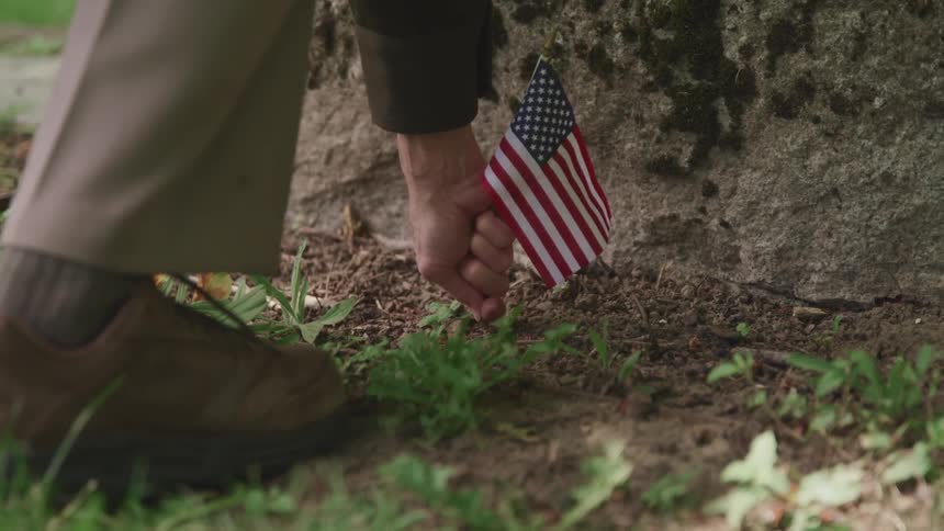 A person planting an american flag on soil with dirt and plants