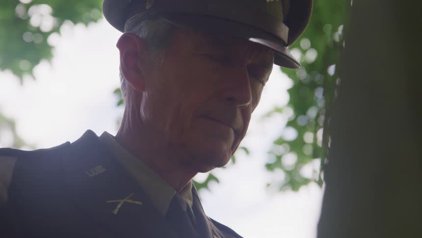 A man in uniform stands outside with his eyes closed
