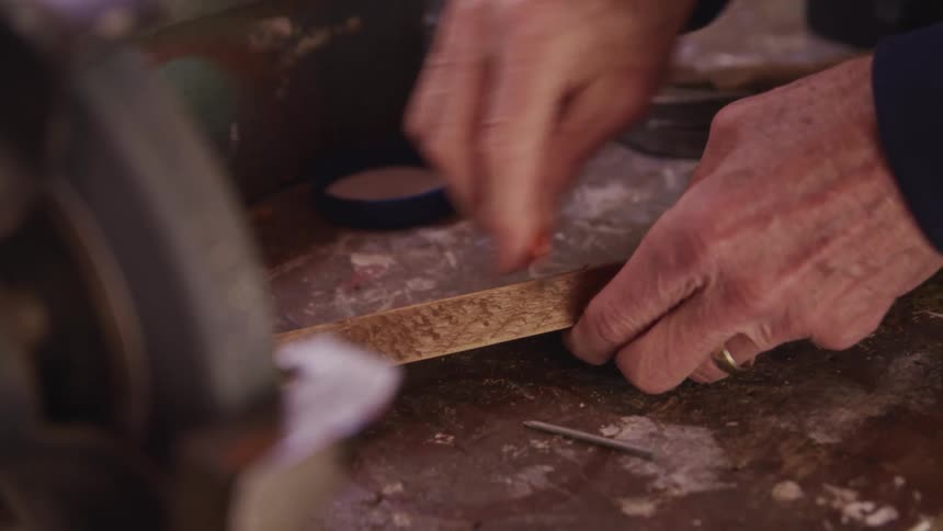 Hands hold a piece of wood and smooth it with a blade on a workbench