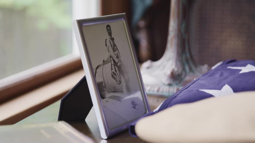 A room with a picture in a frame next to a folded american flag next to a window