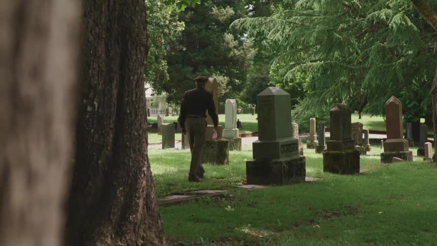 Man wearing officers uniform is walking through a cemetery near grave stones