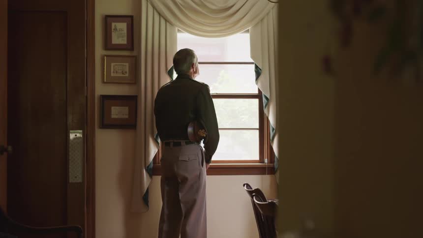 An elderly man at home looking out the window