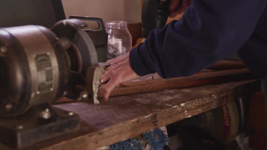 A person using an electrical drill on a plank of wood over a workbench at home