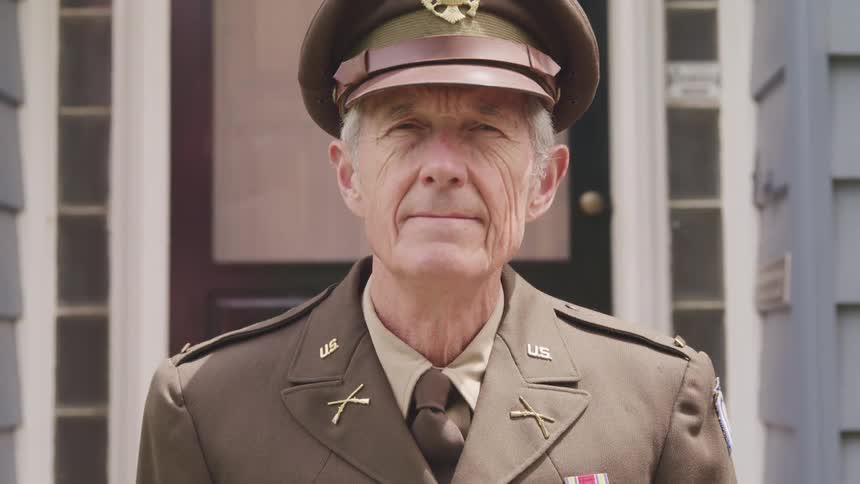 A man in a military uniform standing in front of a house with a door in the background
