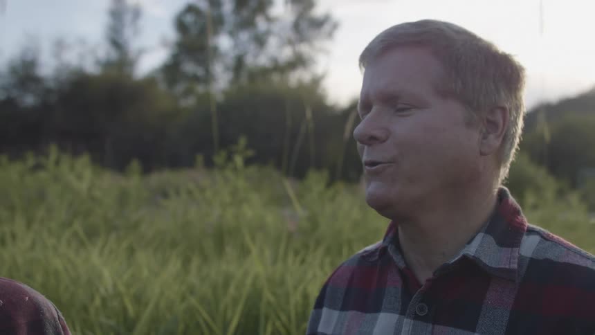 A man stands in the grasslands and talks with someone