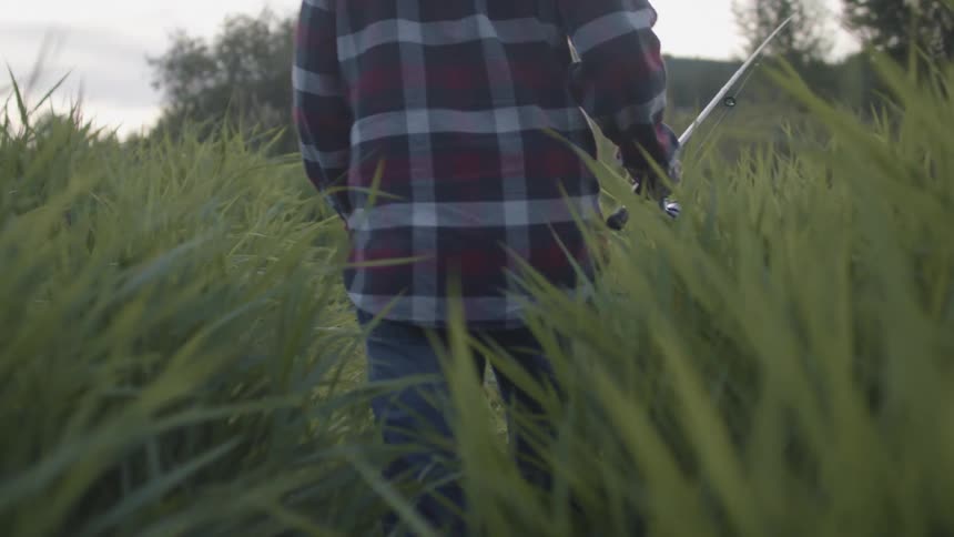A man walks through tall grass carrying a fishing rod