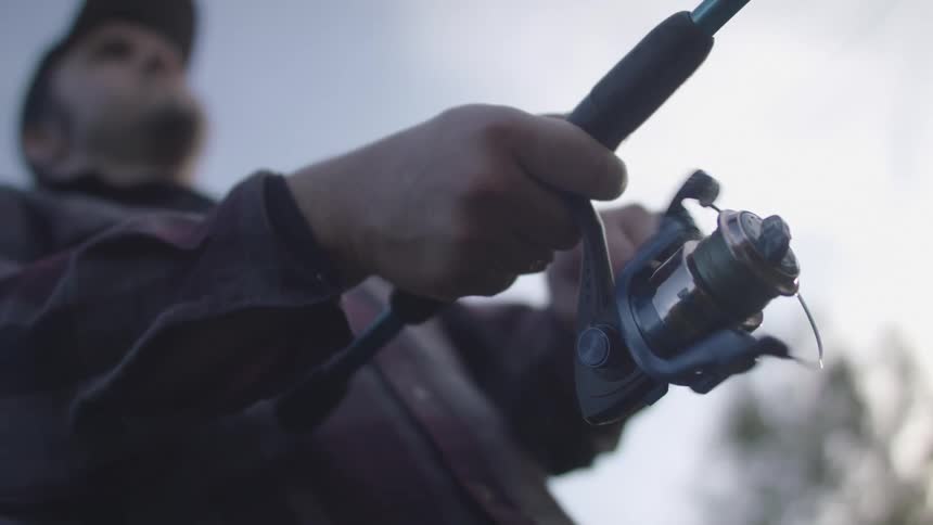 A man slowly turns the handle on the reel of his fishing rod