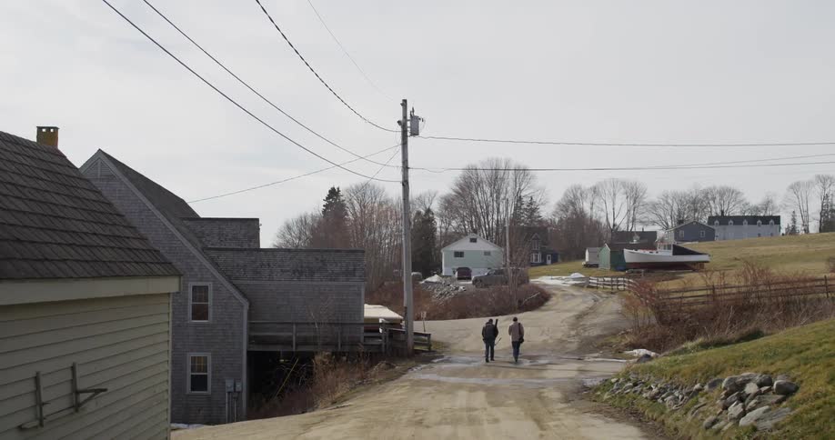 Two people walking down a dirt road past houses on a cold day