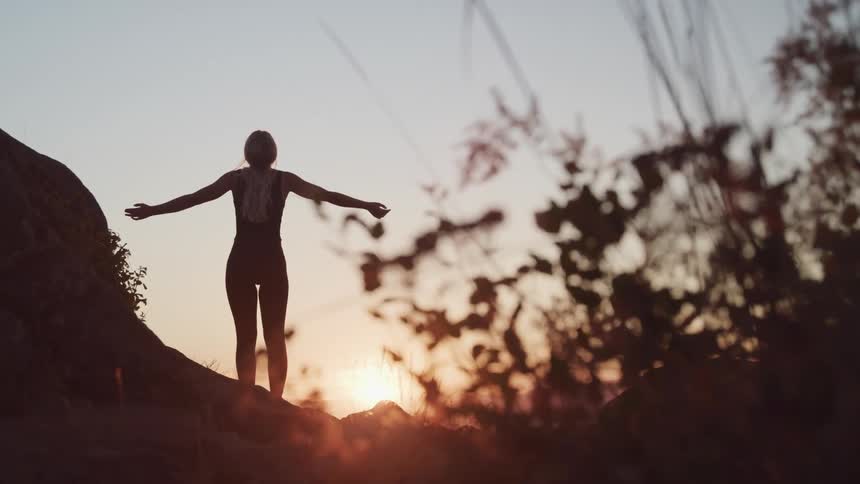 A woman standing outside with her hands stretched out with the sky and clouds in the background
