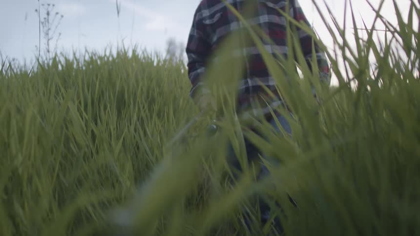 A man carries a fishing rod in front of him as he walks through a grassland