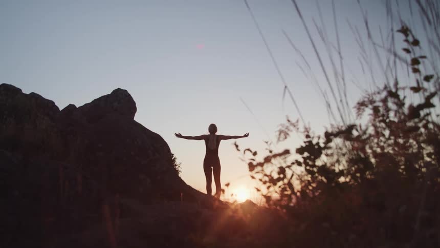 A woman raises her arms up and out as she takes in the view at a canyon at sunset