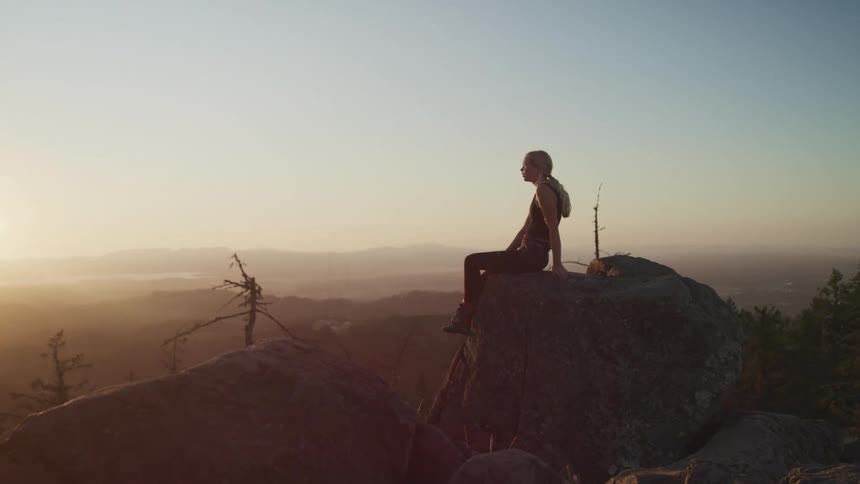 A woman sits on the mountain top as the sun rises