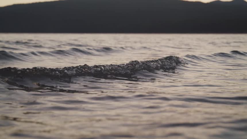 Waves rolling across the water with a mountain in the distance