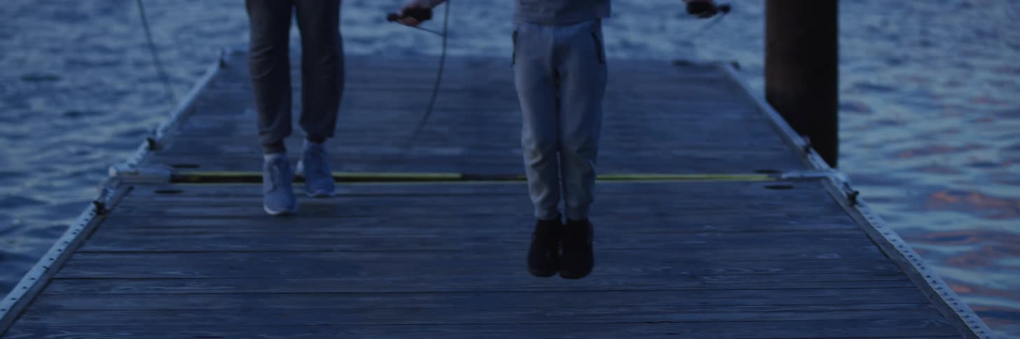 Two people stand on a wooden dock while jumping rope as the sun is down