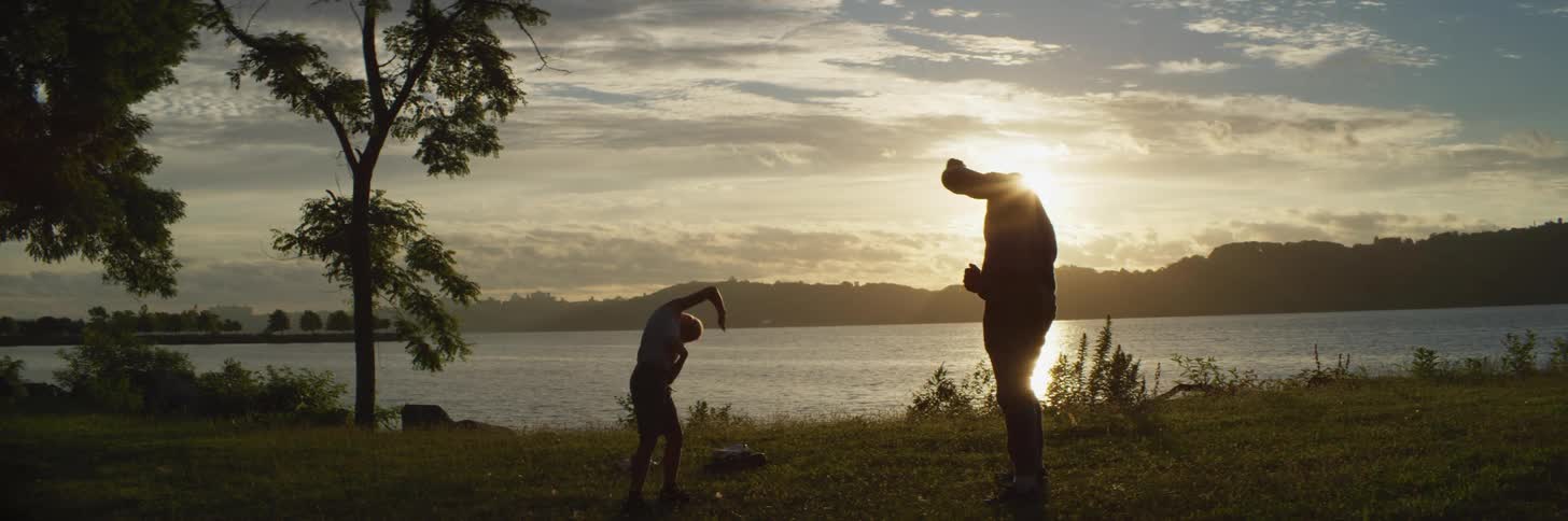 A father and his young son stretch on the shore as the sun sets