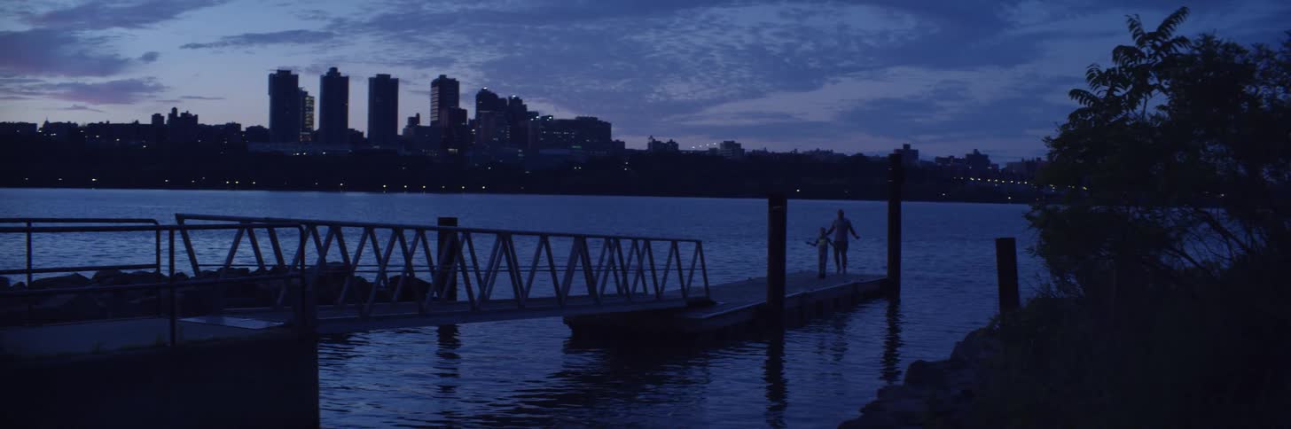 Father and son having fun on a pier in a lake near the city skyline at sunset