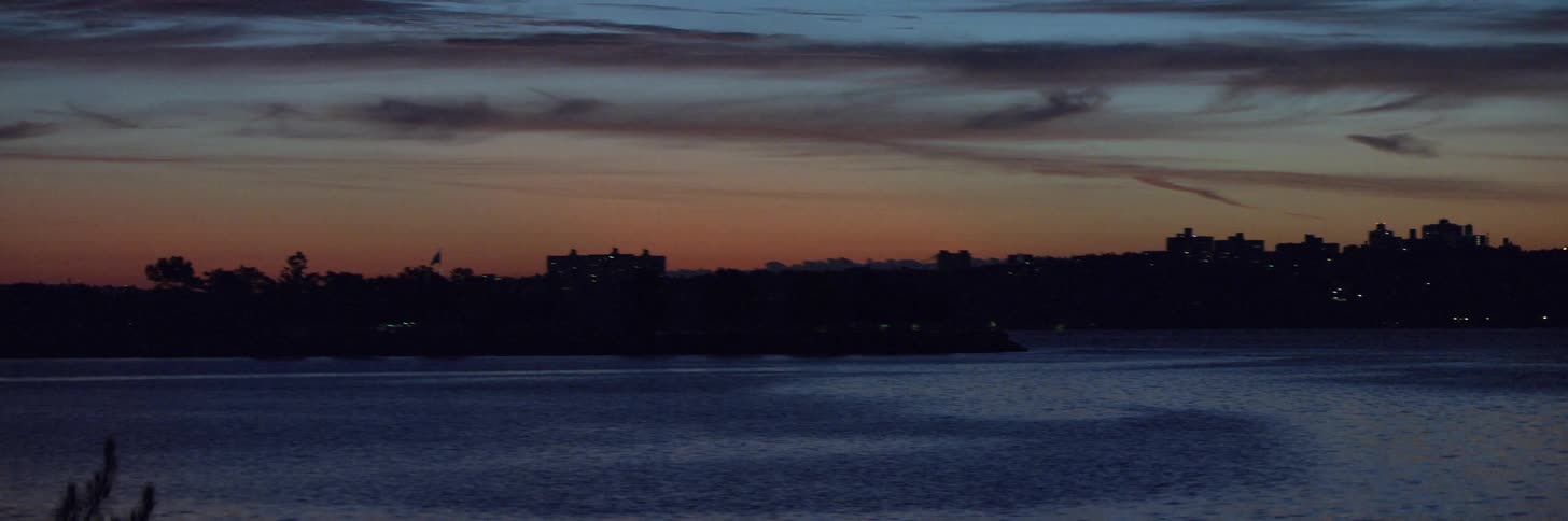 A glowing orange sunset sky over city buildings near shore