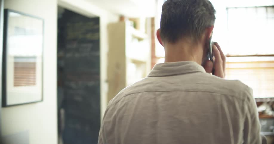 A man talks on a smartphone while walking from one room into a kitchen