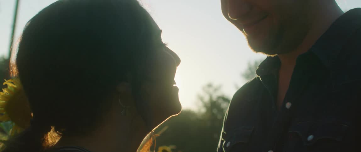 A man kisses a woman on her head and looks down at her and smiles
