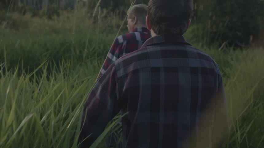Two men walk through the grasslands towards water