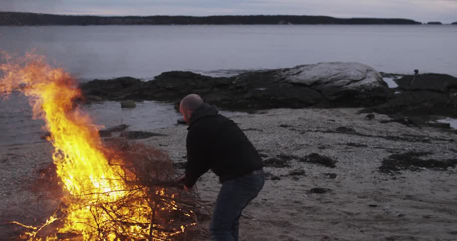 A man puts branches in a campfire