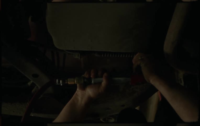 Man works on car undercarriage using power tool