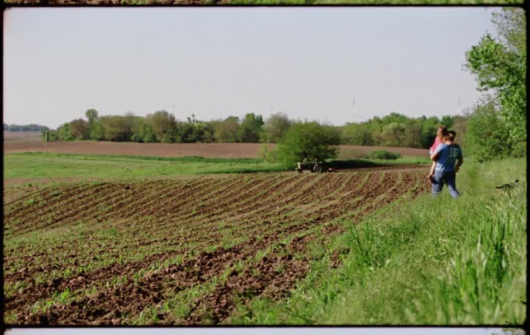 Father carries daugther on his arms while walking on a tiled farm plot