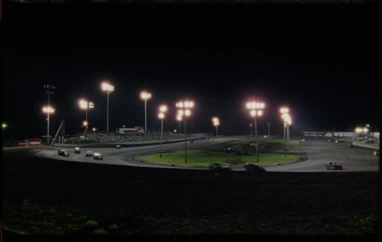 Cars speed around a brightly lit race track at night