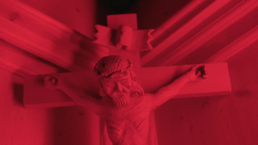 Close up of a crucifix hanging on the corner of a room under a bright red light