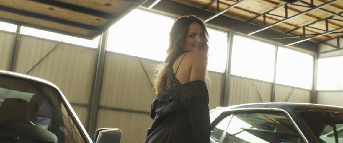 Young woman wearing a coat modeling for the camera near sports cars