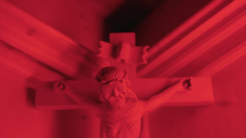 A figure of jesus on a cross sits in the corner of a church under a glowing red light