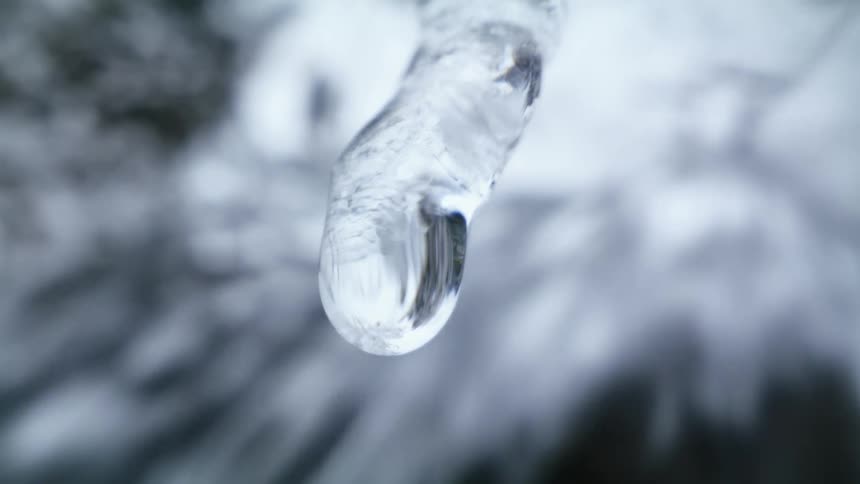 Water drips from an icicle as water flows behind