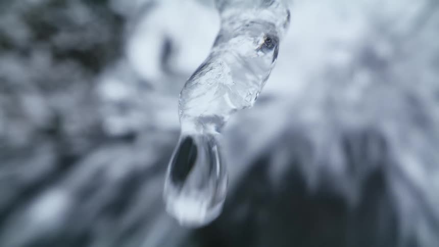 A water drop drips from an icicle with water flowing behind