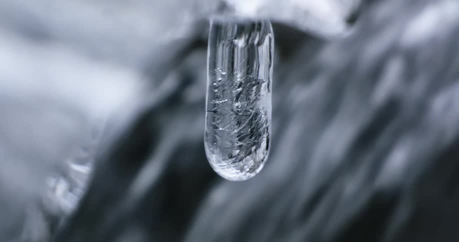 An icicle hanging in front of a rushing waterfall