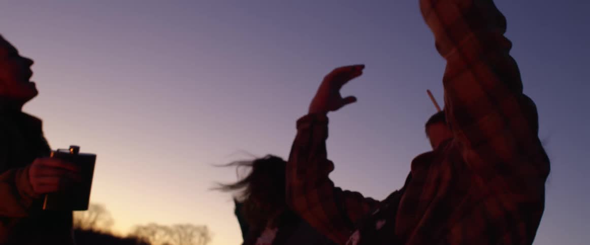 Group of friends smoking and drinking alcohol dancing outdoors at sunset