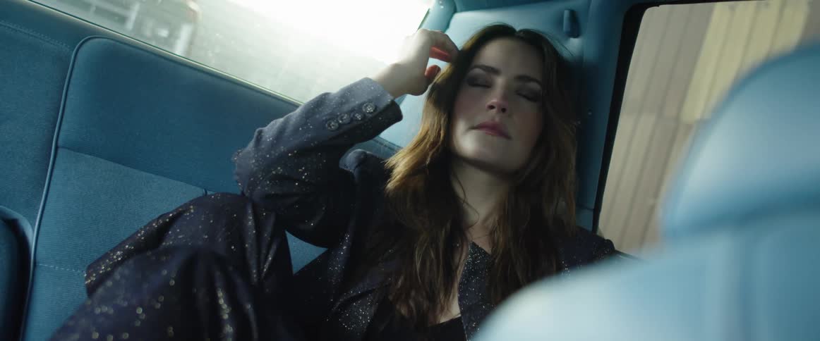 A woman closes her eyes and rests her head in her hands as she sits in the backseat of a vehicle