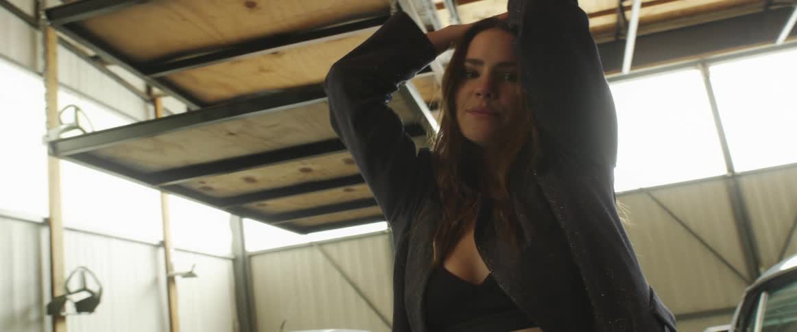 Young long haired woman inside a warehouse walks among the parked cars modeling for the camera