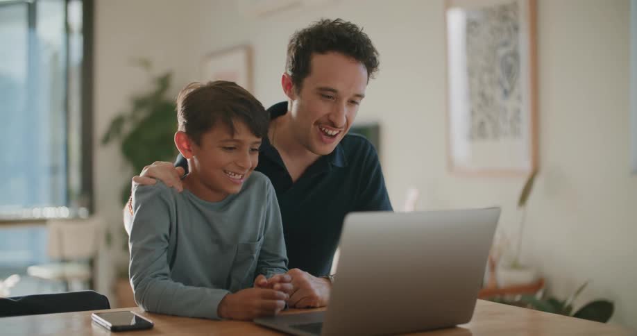 Father and son talking and smiling while using a laptop at home
