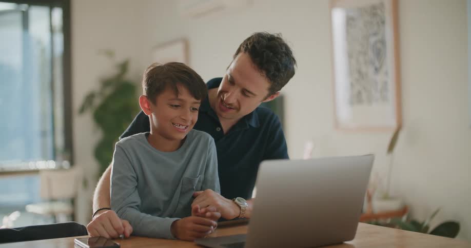 A man and a boy sitting next to a table with a laptop