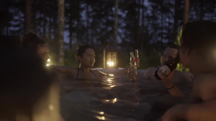 A group of friends enjoy drinks and conversation in a hot-tub outdoors at night