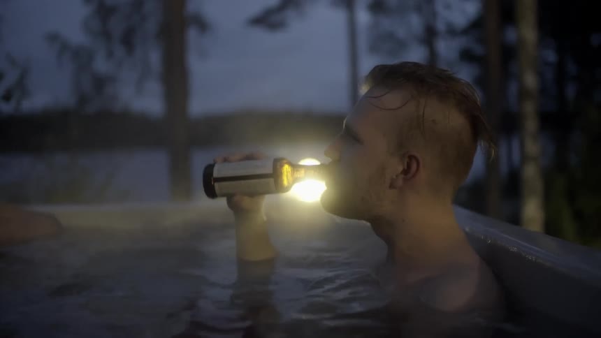 A man sips a beer while relaxing in an outdoor hot tub at night