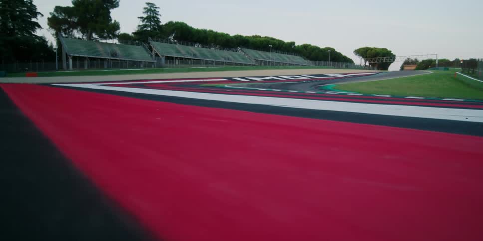 Empty bleachers next to a racing track and grass field on a summer day