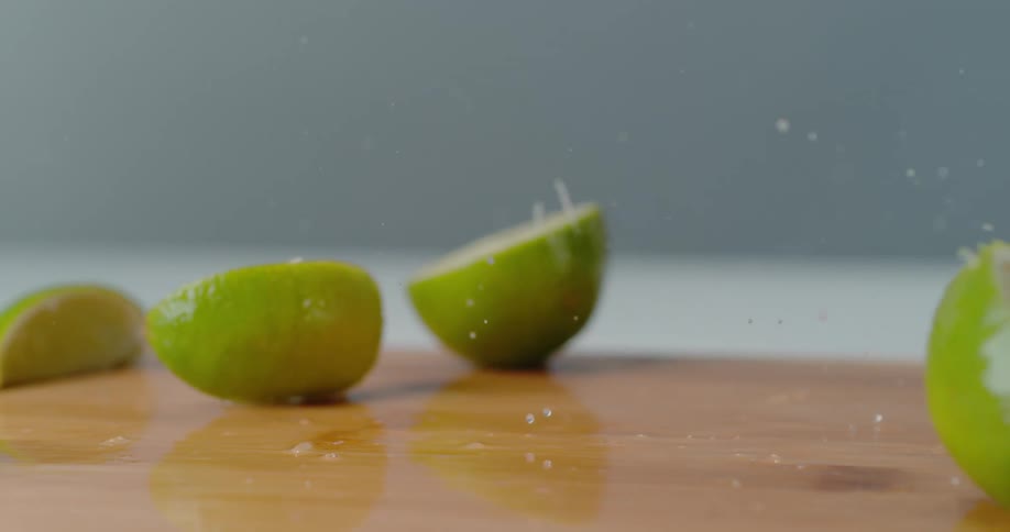Limes are falling onto a table in slow motion