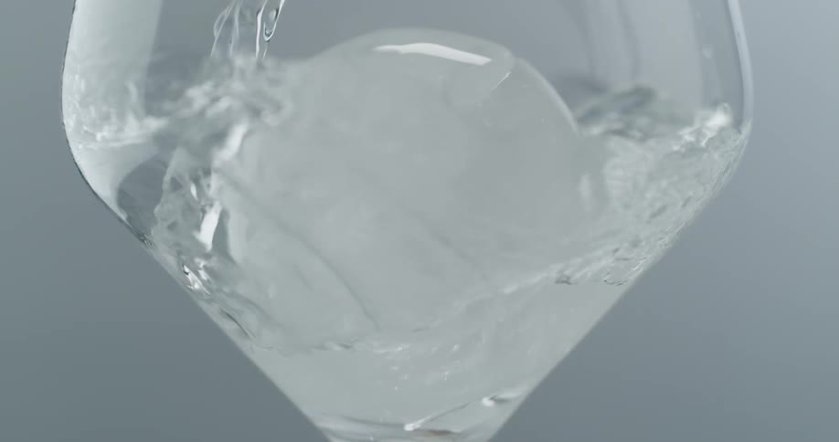 A bottle of clear liquid being poured into a glass with ice
