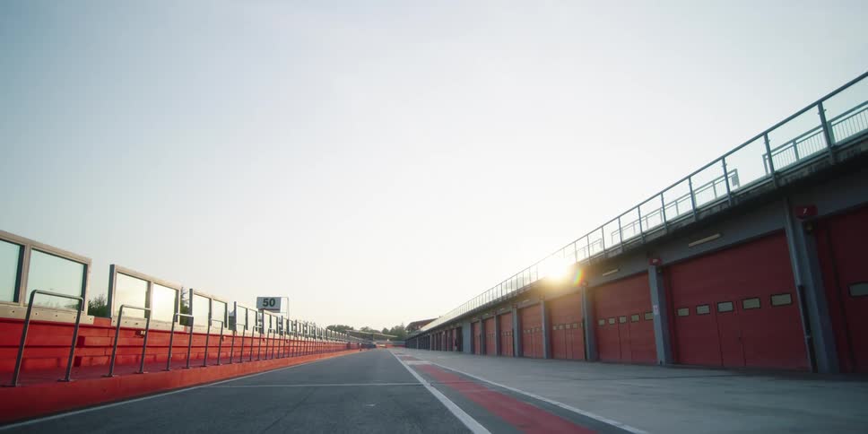 A race track in between red and white bleachers and a building with the sun setting behind it