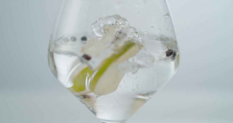 Lemon slices falling into a glass with clear liquid