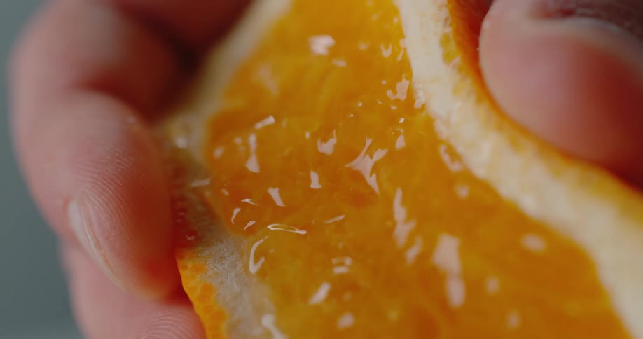 Person squeezes orange sending juice drops spraying into air