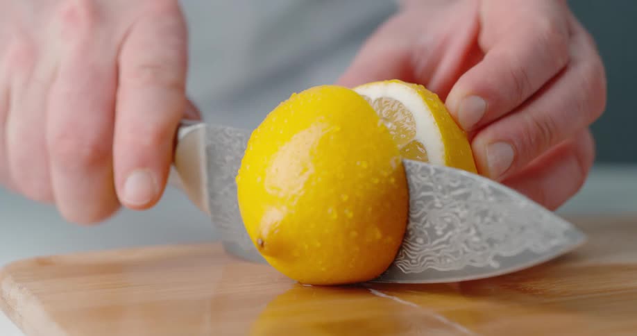 A person is holding a lemon steady with one hand and using a knife to slice it in half with the other hand
