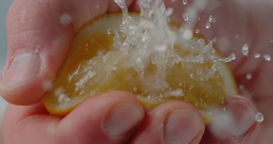 Person squeezes lemon half sending juice drops into the air