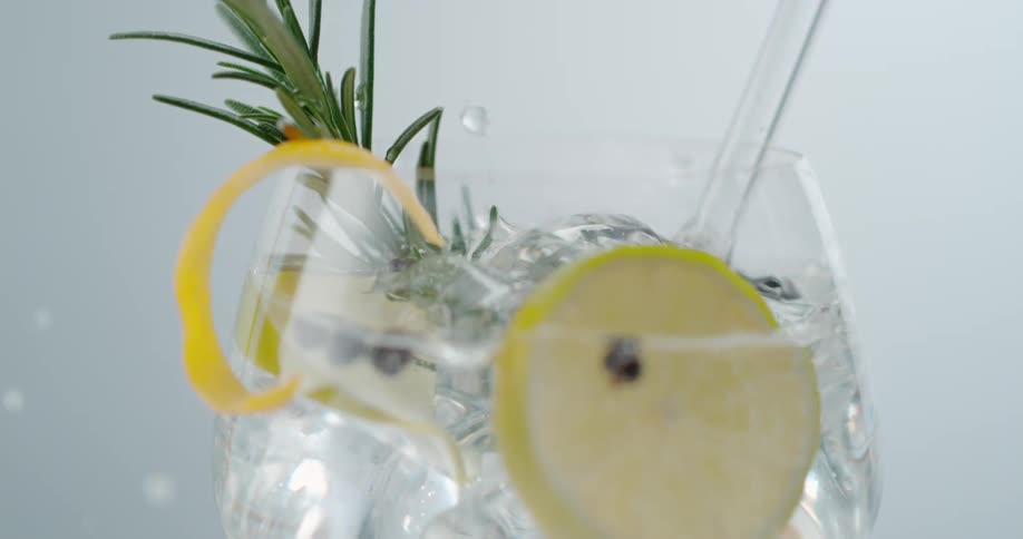 Water splashes up and out as an ice cube is dropped into a full glass of lemon water